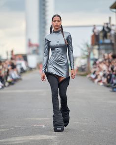 a model walks down the runway in a silver dress with black boots and long hair