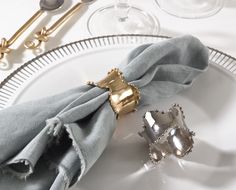 two silver napkins sitting on top of a white plate next to wine glasses and utensils