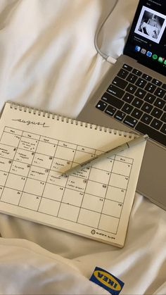 an open laptop computer sitting on top of a bed next to a calendar and pen