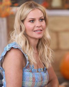 a woman with blonde hair and blue eyes is sitting in front of a pumpkin on the table