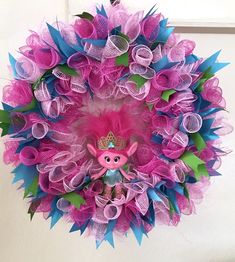 a pink and blue wreath with a trolly doll on it's face hanging from the front door