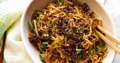 a bowl filled with noodles and meat on top of a white cloth next to chopsticks