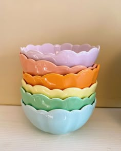 four different colored bowls stacked on top of each other in front of a beige wall