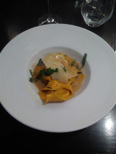 a white plate topped with pasta and veggies next to a glass of wine