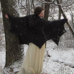 a woman standing next to a tree in the snow wearing a black and white shawl