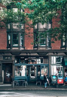 people are sitting at tables in front of a restaurant on the street corner near a tree