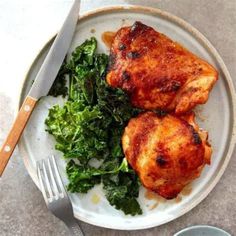 two pieces of chicken on a white plate with greens and a fork next to it