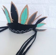 a black and green headpiece with feathers on it's side sitting on a white surface