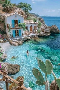 a person swimming in the water next to a house on top of a cliff near the ocean