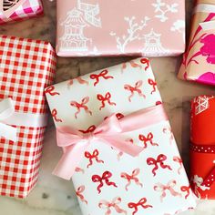 presents wrapped in pink and white paper with bows are on a marble countertop next to other wrapping materials