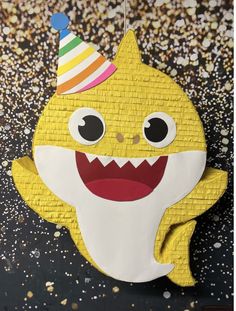 a paper cut out of a yellow shark with a party hat on