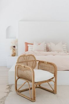 a bed with white sheets and pillows in a bedroom next to a wicker chair