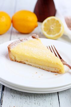 a slice of lemon pie on a white plate with a fork and oranges in the background