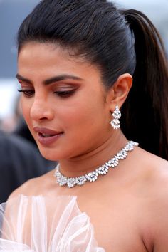 a woman in a white dress wearing a necklace and earrings