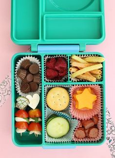 a lunch box filled with fruit, crackers and other snacks on a pink surface