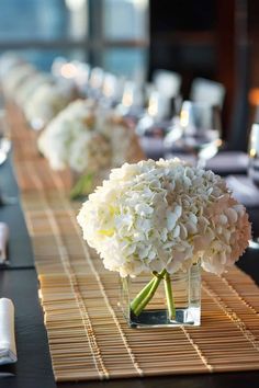 there are many flowers in the vases on this long table with place settings and napkins