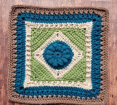 a crocheted square with a blue and green center sits on a wooden surface