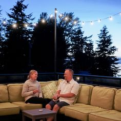 a man and woman sitting on top of a couch next to each other in front of trees