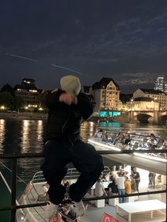 a man on a boat in the water with other boats and buildings behind him at night