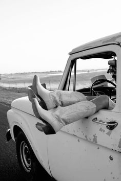 a man laying on the back of an old pickup truck with his feet propped up