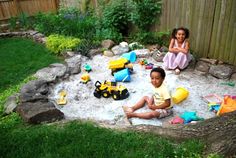 two young children playing in the sand with toy trucks and construction vehicles on it's back yard