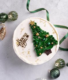 a white cake with green frosting and a christmas tree decoration on the top, surrounded by other holiday decorations