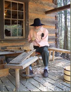 an old man sitting on a wooden bench in front of a log cabin with a window