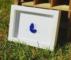 a white frame with a blue butterfly on it sitting in the grass next to some wooden crates