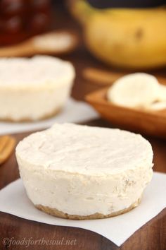 two pieces of cheesecake sitting on top of paper next to bananas and other fruit