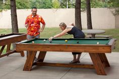 a man and woman playing pool in an outdoor area with ping pong balls on the table