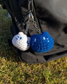 two small crocheted balls are attached to a backpack handle on the grass in front of someone's back pocket