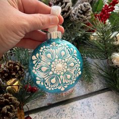 a hand holding a christmas ornament in front of pine cones