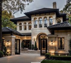 a large white house with lots of windows and lights on the front door, surrounded by trees