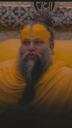 a man with yellow paint on his face and beard sitting in front of a wall