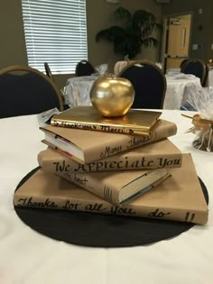 a stack of books sitting on top of a table next to a golden apple in a vase