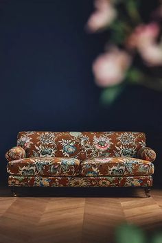 a couch sitting on top of a hard wood floor next to a vase with flowers