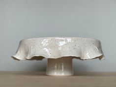 a white ceramic cake dish with speckles on the top, sitting on a wooden table