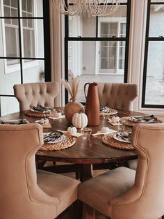 a dining room table set for four with beige chairs and fall decorations on the table