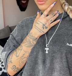 a woman with tattoos on her arm wearing a grey shirt and silver chain bracelets