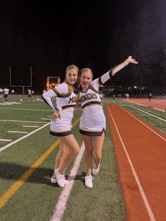 two cheerleaders pose on the field at night