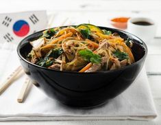 a black bowl filled with noodles and meat on top of a white napkin next to chopsticks