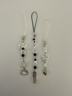 three necklaces with charms attached to them on a white surface, one is black and the other is silver