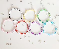 six bracelets with different colored beads and letters are arranged on a white surface next to each other