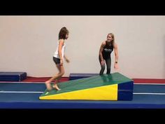 two girls are playing on a trampoline in an indoor gym with blue and yellow mats