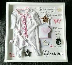 a baby's birth gift is displayed in a white shadow box with pink trim