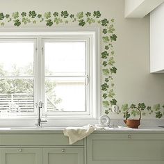 the kitchen is decorated with green leaves and flowers on the wall behind the sink are two windows