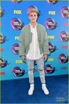 a young man in ripped jeans and a jacket on the blue carpet at an event