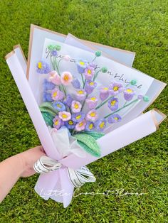 a hand holding a bouquet of flowers on top of a green grass covered field next to an envelope