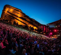 a large group of people at a concert in front of a mountain with lights on it