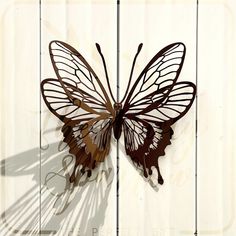 a metal butterfly on a white wooden wall with the shadow of it's wings